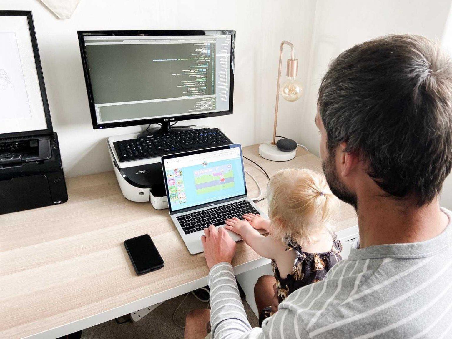 Father working at desktop with child sitting on his lap watching cartoons